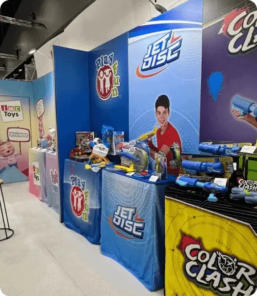 A colorful toy exhibition with various products displayed on tables, featuring brands like Jet Disc and Color Clash against vibrant backdrops.